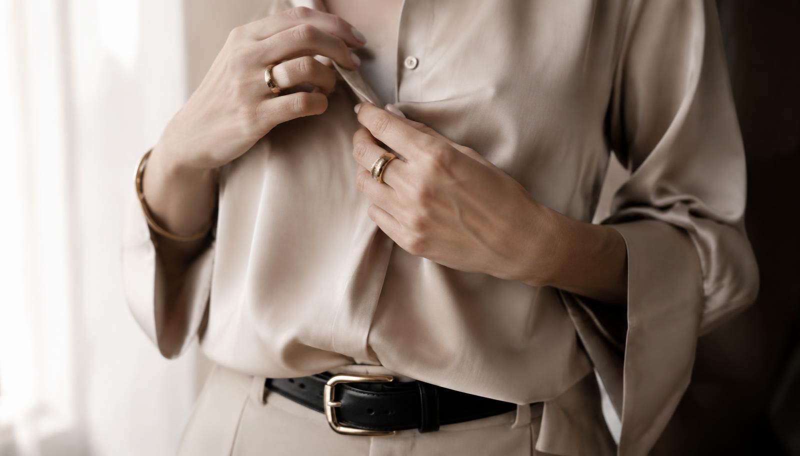 Detalhes de blusa de seda bege com cinto preto e joias douradas